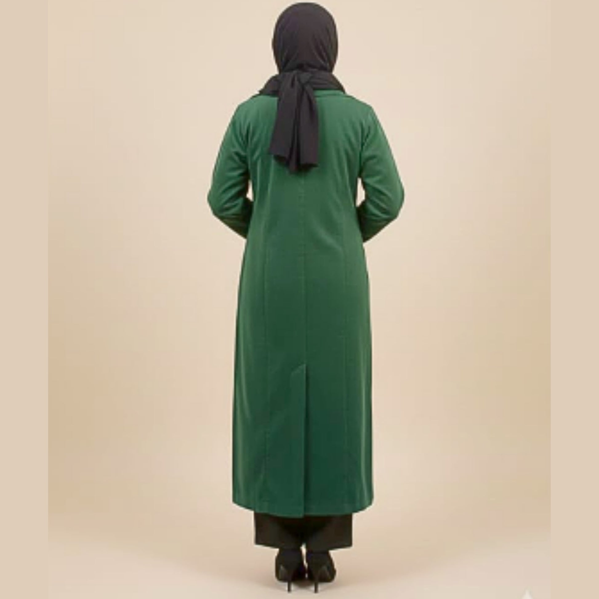 Person wearing a green long coat and black hijab on a beige background