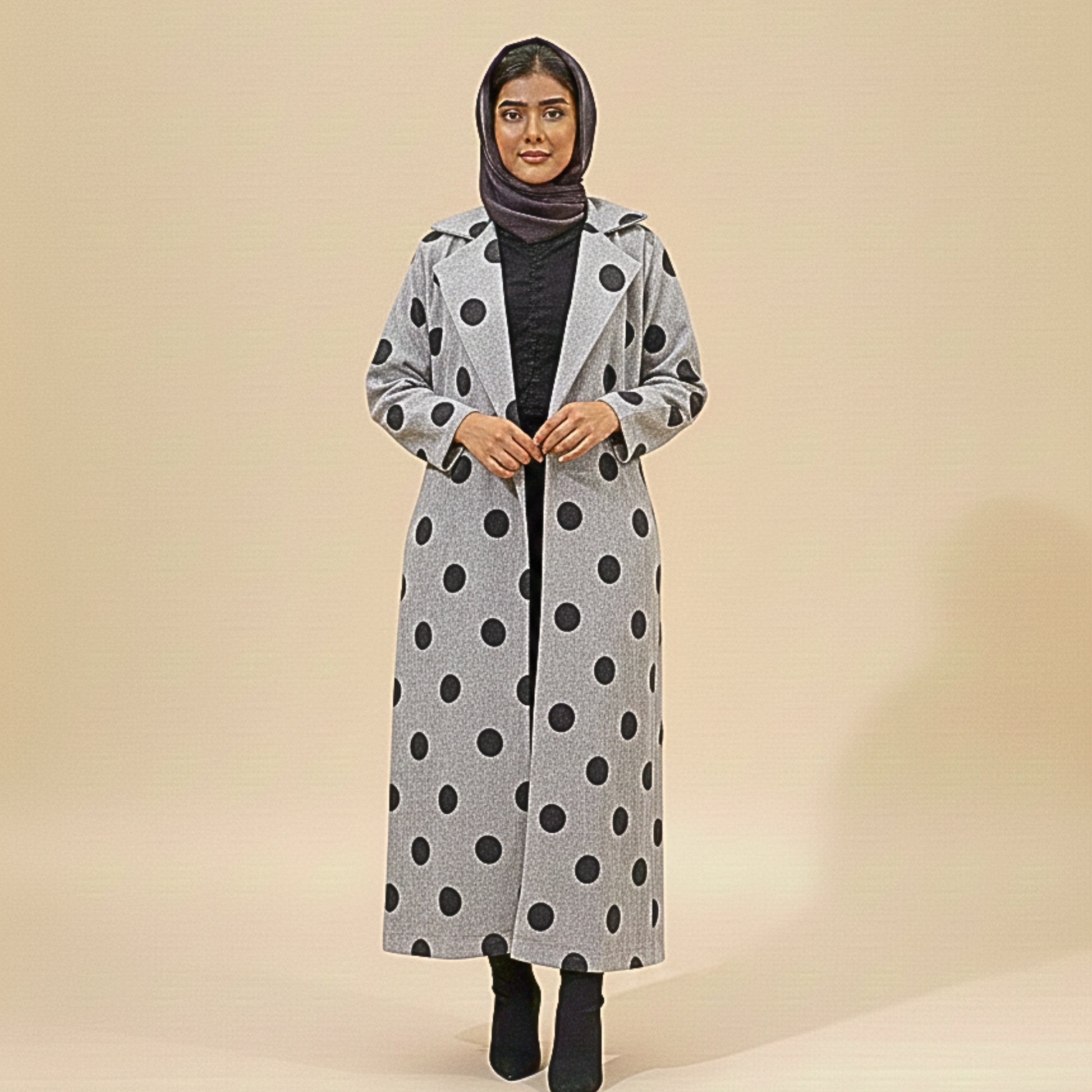 Woman wearing a long gray coat with black polka dots on a beige background